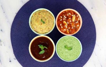 Blue Plate with four small bowls of chutneys in varying colors, yellow, red, green, and brown.