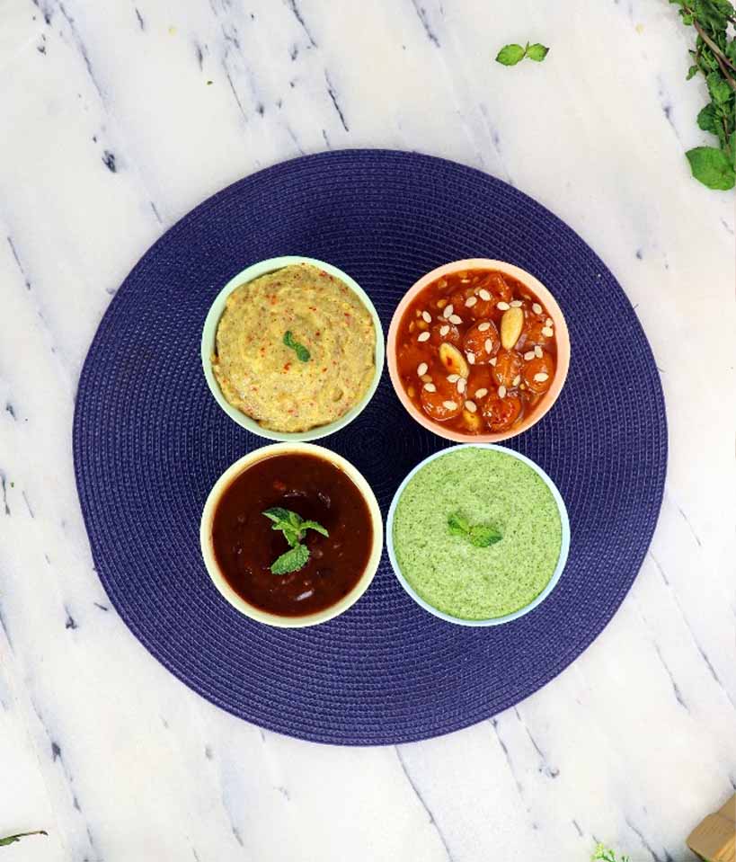 Blue Plate with four small bowls of chutneys in varying colors, yellow, red, green, and brown.